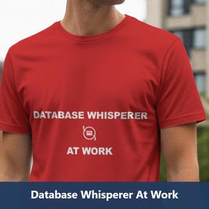 May include: A red t-shirt with the text "DATABASE WHISPERER AT WORK" in white. The shirt has a round neck and short sleeves. The text is centered on the chest.