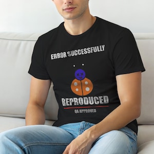 Op de afbeelding: Zwart t-shirt met de tekst "ERROR SUCCESSFULLY REPRODUCED QA APPROVED". Het shirt heeft een cartoon lieveheersbeestje ontwerp met een blauwe kop en een oranje lichaam. Het shirt is gemaakt van een zacht materiaal.