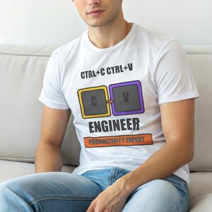 Op de afbeelding: Wit T-shirt met de tekst "CTRL+C CTRL+V" boven een afbeelding van twee computertoetsen, één geel en één paars, met de letters "C" en "V". Onder de afbeelding staat het woord "ENGINEER", met "PRODUCTIVITY EXPERT" eronder.