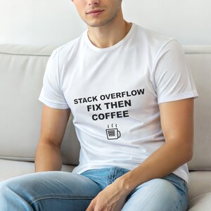 May include: White t-shirt featuring the text "STACK OVERFLOW FIX THEN COFFEE" in black, and a coffee cup graphic. The shirt is paired with blue jeans.
