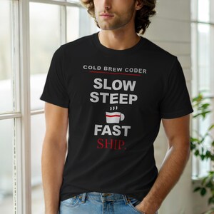 May include: Black t-shirt with the text "COLD BREW CODER" above "SLOW STEEP" and "FAST SHIP." A coffee cup graphic is between "STEEP" and "FAST." The shirt is worn by a person in front of a window.