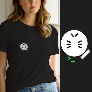 Pode incluir: Uma t-shirt preta de manga curta com um pequeno gráfico circular branco no peito esquerdo. O gráfico retrata um rosto estilizado com olhos e boca fechados, acompanhado por um pequeno retângulo branco e um símbolo de maior que verde com um sublinhado.