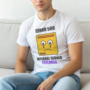 Op de afbeelding: Wit T-shirt met de tekst "ERROR 500" boven een gele computer server afbeelding met een verdrietig gezicht en de woorden "INTERNAL SERVER FEELINGS" in paars. Het shirt wordt door een persoon gedragen.