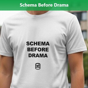 May include: A white t-shirt with the text "SCHEMA BEFORE DRAMA" in black, along with a small graphic. The shirt is being worn outdoors, with a green banner at the top that reads "Schema Before Drama".