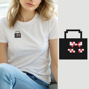 May include: A white short-sleeved t-shirt featuring a small, black, pixelated graphic of a tote bag on the left chest. The bag design includes a simple handle and a decorative pattern of small red and white pixelated squares on its front surface.
