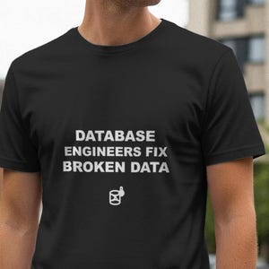 May include: Black crew neck t-shirt with white text that reads "DATABASE ENGINEERS FIX BROKEN DATA". Below the text is a small graphic of a computer icon. The shirt is made of a soft material.