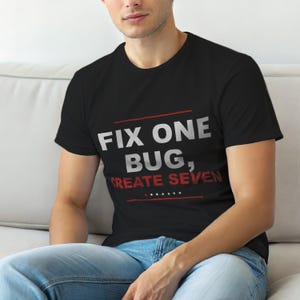 Op de afbeelding: Zwart T-shirt met de tekst "FIX ONE BUG, CREATE SEVEN" in wit en rood. Het shirt heeft een ronde hals en wordt gedragen.