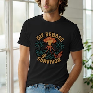 Könnte beinhalten: Schwarzes T-Shirt mit einem Vulkan-Motiv und dem Text "GIT REBASE SURVIVOR". Das Design zeigt einen ausbrechenden Vulkan mit Palmen und Blättern in Orange, Grün und Braun, in kreisförmiger Anordnung.