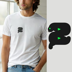 May include: A white short-sleeved t-shirt featuring a small black graphic on the left chest. The graphic is a stylized, rounded black shape resembling a letter S, accented with a bright green circular eye and two small green chevron-shaped markings.