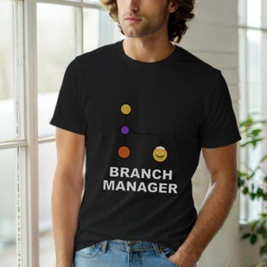 May include: Black crew neck t-shirt with a graphic design. The design features a yellow, purple, and orange dot diagram connected to a smiling face, with the words "BRANCH MANAGER" in white text below.