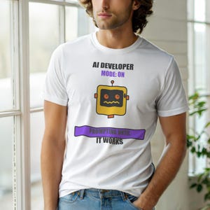 Könnte beinhalten: Weißes T-Shirt mit dem Text "AI DEVELOPER MODE: ON" und einer gelben Roboter-Grafik. Unter dem Roboter befindet sich ein lila Banner mit der Aufschrift "PROMPTING UNTIL IT WORKS".