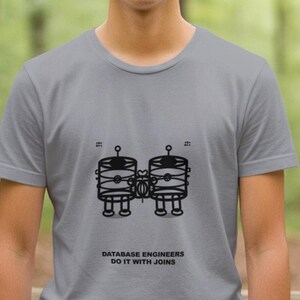 May include: A pale grey t-shirt with a black graphic of two connected database server illustrations. The text "DATABASE ENGINEERS DO IT WITH JOINS" is printed below the graphic. The shirt has short sleeves.