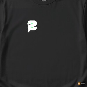 Puede incluir: Camiseta negra con un diseño blanco de un gusano estilizado con ojos verdes. El diseño del gusano está centrado en la camiseta. La camiseta es de algodón grueso.