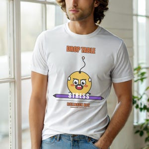 May include: White t-shirt with the text "DROP TABLE" in orange above a cartoon yellow character with the word "STRESS" below. The shirt also has the text "ROLLBACK NOT" in orange.