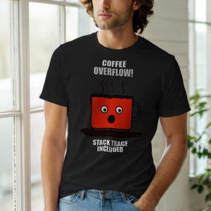 Może przedstawiać: Czarny t-shirt z napisem "COFFEE OVERFLOW!" nad rysunkową filiżanką kawy z zaskoczoną miną. Pod filiżanką znajduje się napis "STACK TRACE INCLUDED". Filiżanka jest czerwona, a z niej unosi się para.