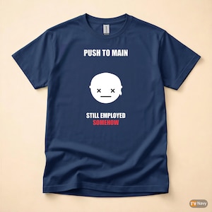 May include: Navy blue t-shirt with the text "PUSH TO MAIN" above a white graphic of a face with crossed-out eyes and a horizontal line for a mouth. Below the graphic, the text reads "STILL EMPLOYED SOMEHOW" in red.