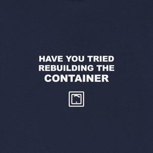 May include: Navy blue t-shirt with white text that reads "HAVE YOU TRIED REBUILDING THE CONTAINER" and a small square graphic. The shirt is a solid color and has short sleeves. The text is centered on the front of the shirt.