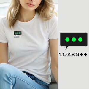Könnte beinhalten: Ein weißes kurzärmeliges T-Shirt mit einer kleinen schwarzen rechteckigen Sprechblasengrafik auf der linken Brust. Die Grafik enthält drei leuchtend grüne Punkte und den Text TOKEN++ in einer schwarzen serifenlosen Schrift.
