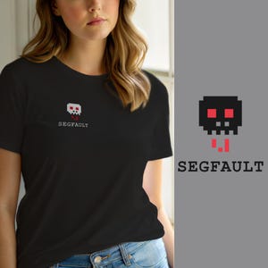 Op de afbeelding: Een zwart T-shirt met korte mouwen en een kleine, gepixelde schedelafbeelding op de linkerborst. De schedel is wit met rode ogen en rode accenten eronder. De tekst "SEGFAULT" is in een wit, monospaced lettertype onder de schedel gedrukt.