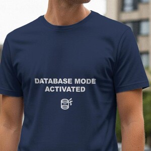 Może przedstawiać: Granatowa koszulka z białym napisem "DATABASE MODE ACTIVATED" i ikoną bazy danych. Koszulka ma okrągły dekolt.