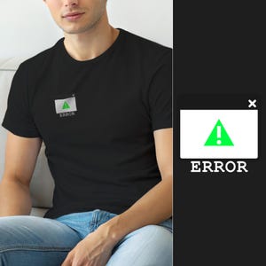 Op de afbeelding: Een zwart T-shirt met korte mouwen en een kleine afbeelding op de borst. De afbeelding is een wit rechthoekig computervenster met een foutmelding, een groen driehoekje met een wit uitroepteken en het woord ERROR in witte letters eronder.