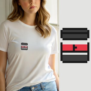 Peut inclure: Un t-shirt blanc à manches courtes avec un petit graphique en pixel art centré sur la poitrine. Le motif se compose d'une barre rectangulaire gris foncé en haut, d'une section centrale rouge vif avec un petit carré noir et d'une barre inférieure.