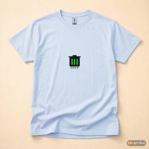 May include: Light blue t-shirt with a black and green graphic of a trash can and the word "DROP" printed below. The shirt is made of a soft material and has short sleeves.