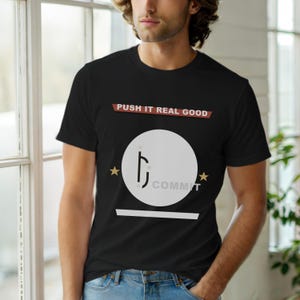 Puede incluir: Camiseta negra de cuello redondo con el texto "PUSH IT REAL GOOD" en rojo y blanco. La camiseta presenta un círculo blanco con un diseño estilizado y la palabra "COMMIT" debajo. Dos estrellas doradas flanquean el círculo.