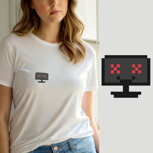 Op de afbeelding: Een wit T-shirt met korte mouwen en een kleine pixel art afbeelding op de borst. De afbeelding toont een zwarte computermonitor met een standaard en twee rode, gepixelde X-symbolen als ogen op het scherm, tegen een effen witte achtergrond.