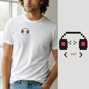 May include: A white short-sleeved t-shirt featuring a small pixel art graphic on the left chest. The design consists of black headphones with red ear cups and a small red pixelated mouth symbol underneath, rendered in a simple digital style.