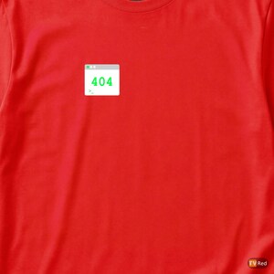 May include: A bright red t-shirt featuring a small graphic of a 404 error message in a window. The error message is displayed in green text on a white background. The shirt is made of a soft material.