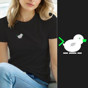 Op de afbeelding: Een zwart t-shirt met korte mouwen en een kleine afbeelding op de borst. De afbeelding toont een witte gestileerde vogel met een felgroene snavel, een groene staart en een klein grijs vleugeldetail, geplaatst boven een witte stippellijn.