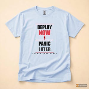 May include: Pale blue t-shirt featuring the text "DEPLOY NOW, PANIC LATER" in black and red. The shirt also includes the words "DEVOPS CONFIDENCE". The t-shirt is made of a soft material.