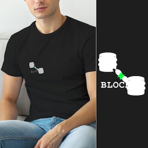 May include: A black short-sleeved t-shirt featuring a white graphic on the chest. The graphic depicts two white cylindrical shapes connected by a small green link, with the white text "BLOCK" printed horizontally across the lower section.