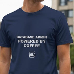 Può includere: T-shirt blu navy con testo bianco "DATABASE ADMIN POWERED BY COFFEE" e grafica tazza di caffè. La maglietta a maniche corte è realizzata in materiale morbido.