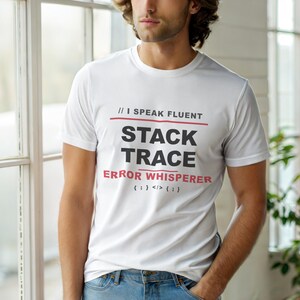 Può includere: T-shirt bianca con la scritta "// I SPEAK FLUENT STACK TRACE ERROR WHISPERER {;} </>{;}" in nero e rosso. La maglietta è indossata da una persona con jeans blu.