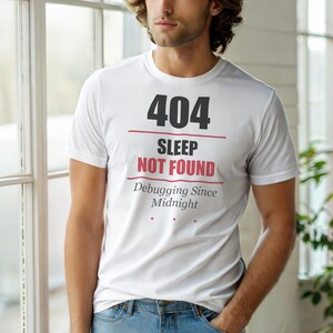 Könnte beinhalten: Weißes T-Shirt mit dem Text "404 Sleep Not Found" in Schwarz und Rot. Darunter steht "Debugging Since Midnight". Das T-Shirt hat einen Rundhalsausschnitt.