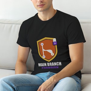 Op de afbeelding: Zwart T-shirt met een schildontwerp. Het schild is goudkleurig met een oranje binnenkant, met een gestileerde scooter en een paars hangslot. De tekst "MAIN BRANCH GUARDIAN" staat eronder in wit en paars.