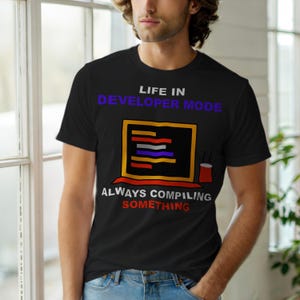 May include: Black t-shirt with the text "LIFE IN DEVELOPER MODE" above a graphic of a computer screen with code and the text "ALWAYS COMPILING SOMETHING". A red coffee cup is next to the computer screen.