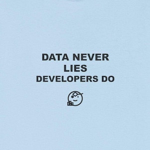 May include: A light blue t-shirt with the text "DATA NEVER LIES DEVELOPERS DO" in black, along with a small graphic of a smiling face. The shirt has short sleeves and a crew neck.