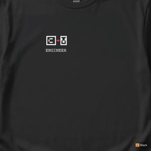 May include: Black t-shirt with the word "ENGINEER" beneath a pixelated graphic. The graphic consists of two white squares, one with a red plus sign. The shirt is made of heavy cotton.