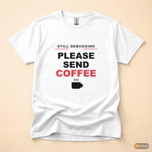 May include: White t-shirt with the text "STILL DEBUGGING PLEASE SEND COFFEE" in black and red. A black coffee cup icon is below the text. The shirt is made of a soft material.