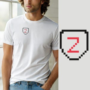 Op de afbeelding: Een wit T-shirt met korte mouwen en een kleine pixel art afbeelding op de linkerborst. De afbeelding bestaat uit een zwart omlijnde schildvorm met daarin een rode, gepixelde letter Z. Het T-shirt heeft een ronde hals en een standaard pasvorm.