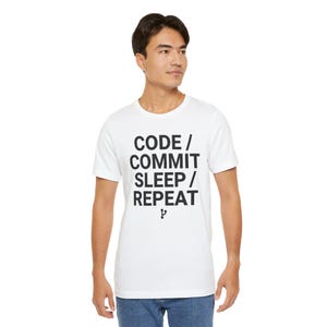 May include: White t-shirt with the text "CODE / COMMIT / SLEEP / REPEAT" in black, a humorous design for programmers. The shirt is made of a soft material and is suitable for casual wear.