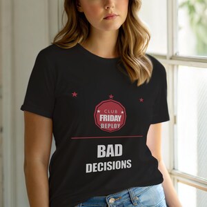 Könnte beinhalten: Schwarzes T-Shirt mit dem Text "CLUB FRIDAY DEPLOY" in einem rot-weißen kreisförmigen Design und den Worten "BAD DECISIONS" in Weiß. Das Shirt hat drei kleine rote Sterne über dem Text.