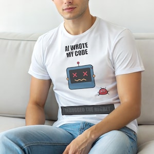 Puede incluir: Camiseta blanca con el texto "AI WROTE MY CODE" sobre un robot de dibujos animados con ojos en "X" y una boca triste. Debajo, el texto "I DEBUGGED THE REGRET". Un pequeño insecto rojo está a la derecha del robot.