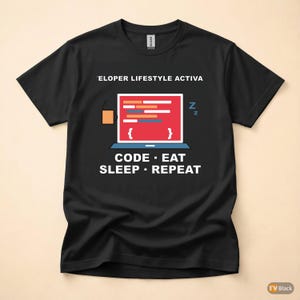 Op de afbeelding: Zwart t-shirt met een afbeelding van een laptop met code, een koffiekopje en de tekst "ELOPER LIFESTYLE ACTIVA" en "CODE • EAT • SLEEP • REPEAT" in het wit. Het ontwerp bevat een slaapsymbool.