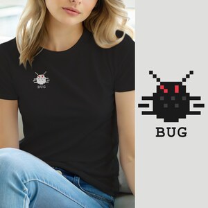 Op de afbeelding: Een zwart t-shirt met een kleine, gepixelde afbeelding van een zwart insect met rode ogen en voelsprieten op de linkerborst. Onder de afbeelding van het insect staat het woord BUG in een wit, blokkerig pixel-lettertype gedrukt.