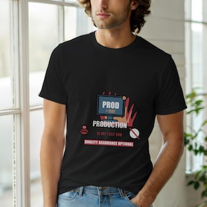 Può includere: T-shirt nera con un design grafico raffigurante uno schermo di computer con la scritta "PROD = TEST" e "PRODUCTION IS MY TEST ENV". Il design include un elemento a forma di fiamma rossa e arancione e un piccolo insetto.