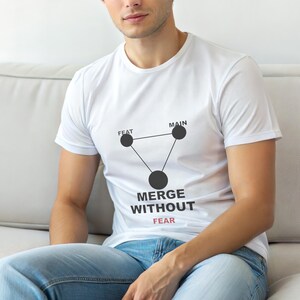 Puede incluir: Camiseta blanca con un gráfico negro de un triángulo con tres círculos y las palabras "MERGE WITHOUT FEAR" en negro y "FEAR" en rojo. La camiseta está hecha de un material suave.